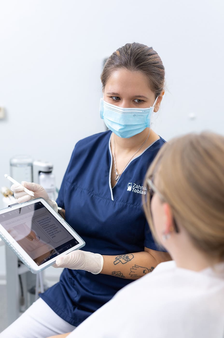 Eine Dentalhygienierin zeigt einer Patientin eine Informationsslide auf einem Tablet